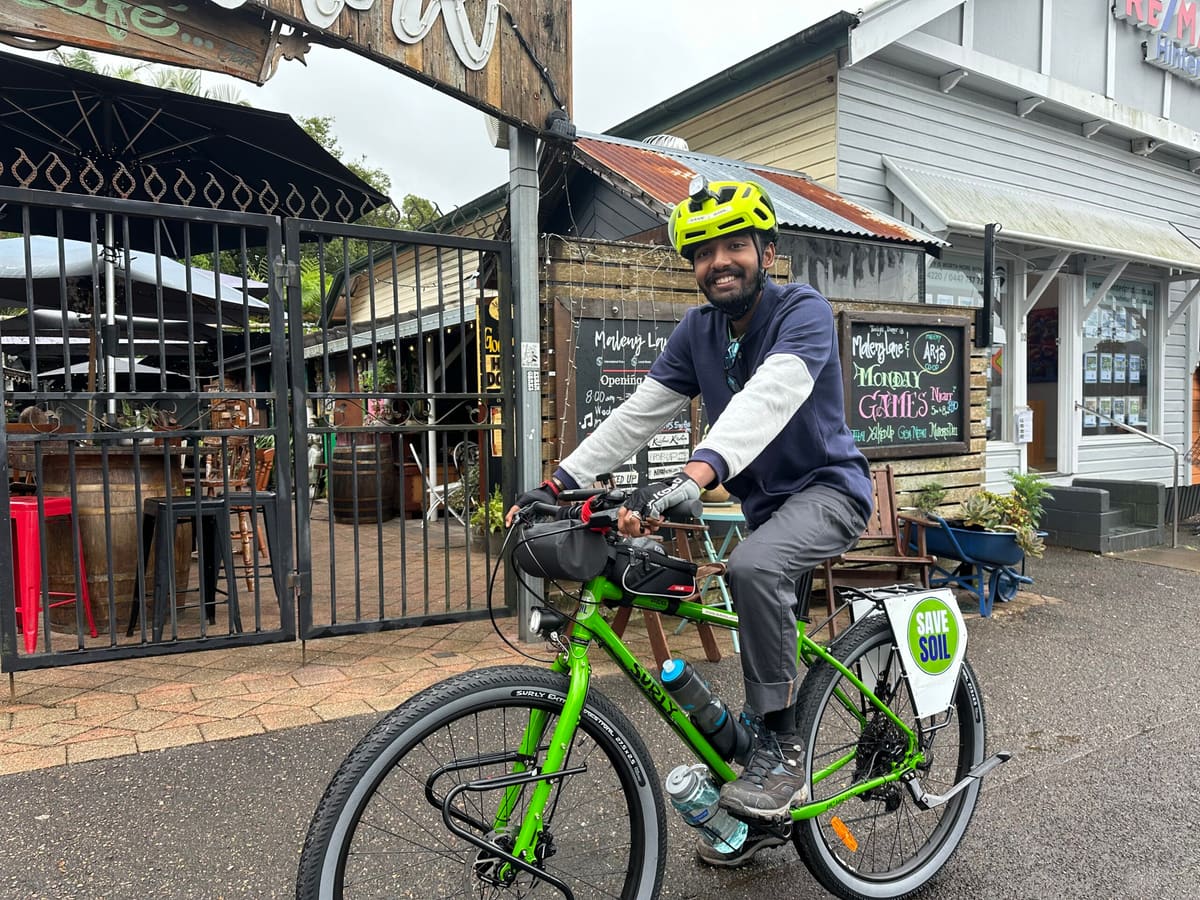 Sahil Jha in his cycling helmet riding his loaded bicycle past a café in Queensland