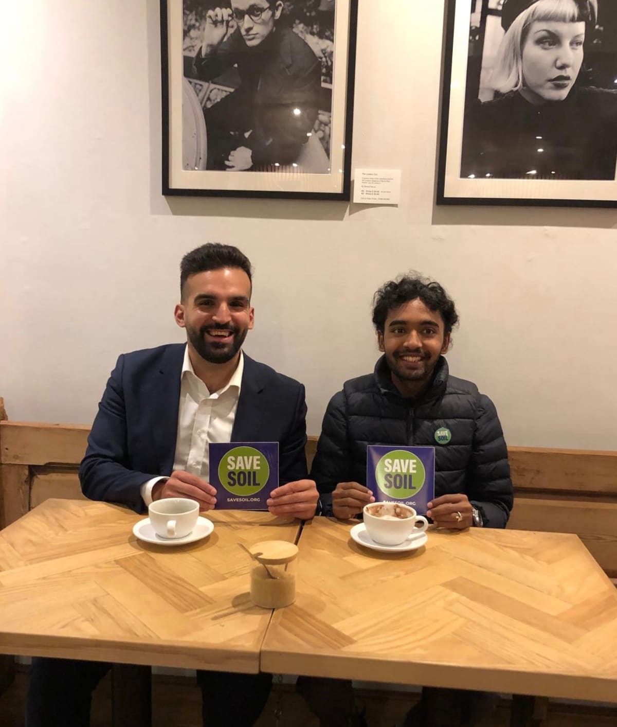 Sahil Jha and Mete Coban holding Save Soil cards at a café table