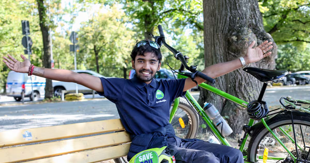 Sahil Jha sitting on a bench with arms outstretched beside his bicycle at Hanover’s Maschsee lake